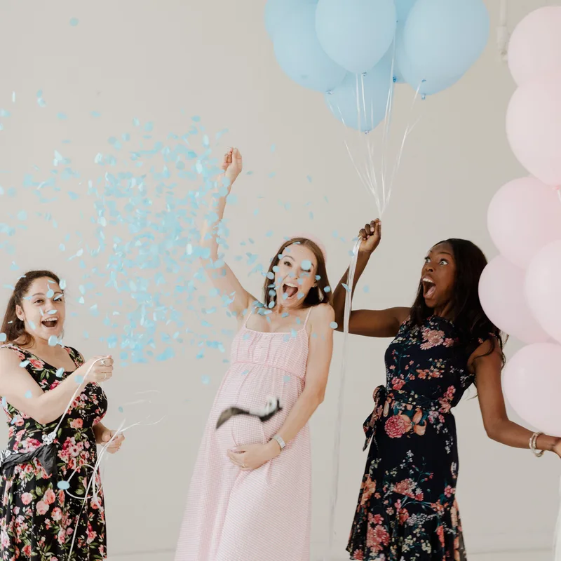 Friends celebrating a gender reveal with balloons and blue confetti, the kind of guest photos EventSnap collects